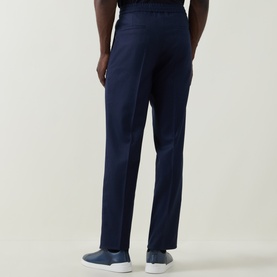 Model wearing Brunello Cucinelli Blu Marina wool trousers, rear view, styled with blue low-top trainers.
