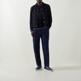 Model wearing Brunello Cucinelli Blu Marina virgin wool trousers, styled with a navy jacket, t-shirt and navy trainers.