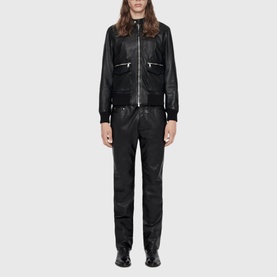 Model wearing All Saints black leather bomber jacket and matching black leather trousers with silver zip detail and black ankle boots.