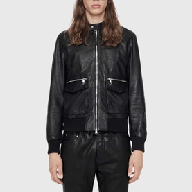 Model wearing All Saints black leather bomber jacket with zip chest pockets and ribbed cuffs, collar, and hem, styled with black trousers.