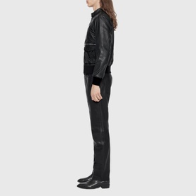 Model wearing All Saints black leather bomber jacket with matching black leather trousers and black Chelsea boots, side profile view.
