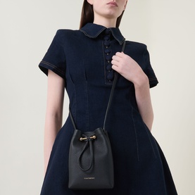 Model carrying Strathberry Osette Midi Pouch Bag in black grained leather with gold-tone drawstring hardware, worn on narrow crossbody strap, styled