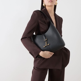 Model carrying Strathberry Kite Hobo Bag in black grained calf leather with gold-toned hardware, styled with a dark brown suit.