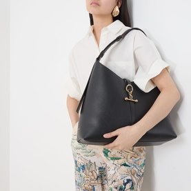 Model carrying Strathberry Kite Maxi Hobo Bag in black grained leather with gold-toned hardware and signature bar closure, worn on shoulder.