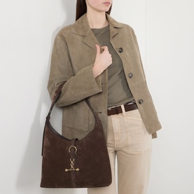 Model carrying Strathberry Kite Suede Hobo Bag in chocolate, gold-tone hardware and ring detail, styled with suede jacket and tailored trousers.