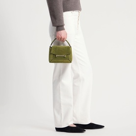 Model carrying Strathberry Mosaic Nano Top Handle Bag in lime/khaki suede, gold-tone hardware, styled with white wide-leg trousers and black flats.