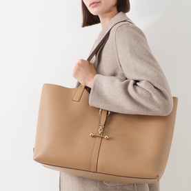 Model carrying Strathberry Kite Leather Tote Bag in caramel, double shoulder straps, gold-tone Music Bar hardware, grained finish
