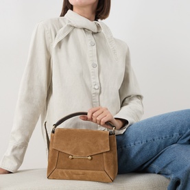 Model carrying Strathberry Mosaic Top Handle Bag in Toffee/Espresso suede, with top handle and gold-tone hardware, styled with cream shirt and jeans