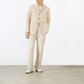 Model wearing Thom Browne beige cotton blazer styled with matching trousers and white trainers.