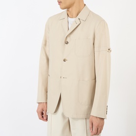 Model wearing Thom Browne beige cotton blazer with three-button front, patch pockets, and arm tab detail, styled with matching trousers.