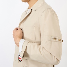 Model wearing Thom Browne beige cotton blazer, close-up showing button cuffs and signature red, white and blue stripe trim detail.
