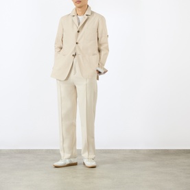 Model wearing Thom Browne beige cotton blazer styled with matching trousers and white trainers.