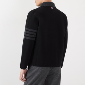 Model wearing Thom Browne black wool casual jacket, rear view, with signature four-bar grey stripe detail on left sleeve and ribbed collar.