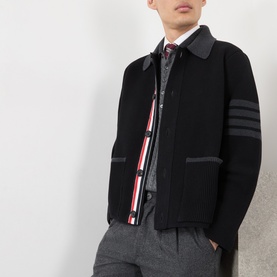 Model wearing Thom Browne black wool casual jacket with 4-bar stripe sleeves and red-white zip tape, styled with grey trousers and tie