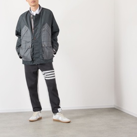 Model wearing Thom Browne Tech Field Jacket in dark grey with contrast stripe fabric, styled with matching joggers and white trainers.