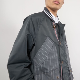 Model wearing Thom Browne Tech Field Jacket in dark grey with contrast pinstripe panels, shawl collar with tipped stripe detail and button fastening.
