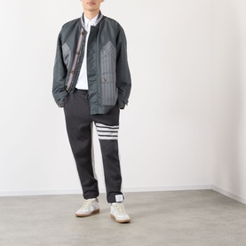 Model wearing Thom Browne Tech Field Jacket in dark grey with contrast stripe detail, styled with black trousers, striped socks and white trainers.