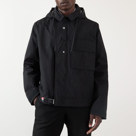 Model wearing Thom Browne Mariner Technical Jacket in black with detachable hood, chest pocket, and signature stripe loop tab.