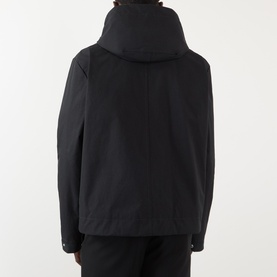 Model wearing Thom Browne Mariner Technical Jacket in black, rear view showing detachable hood with drawstring and adjustable cuffs.
