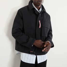 Model wearing Thom Browne Mariner Technical Jacket in black, showing signature stripe loop tab on chest pocket, styled with striped shirt underneath.
