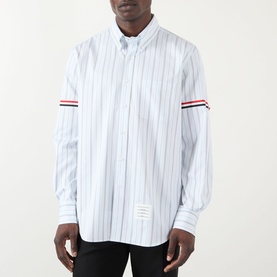Model wearing Thom Browne medium grey pinstripe cotton shirt with signature red, white and blue grosgrain armband detail.