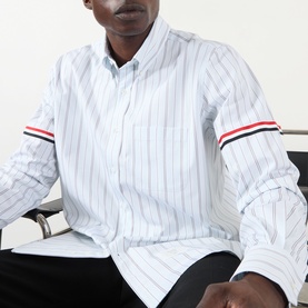 Model wearing Thom Browne medium grey striped cotton casual shirt with signature red, white and blue grosgrain armband detail.