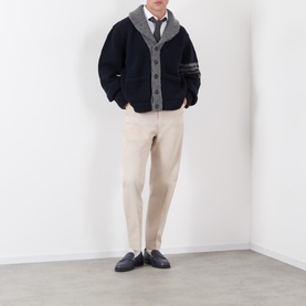 Model wearing Thom Browne Tapered Pressed-Crease Chinos in beige, styled with a navy cardigan, tie and black loafers
