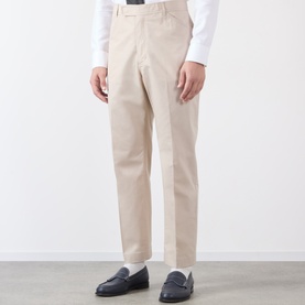 Model wearing Thom Browne Tapered Pressed-Crease Chinos in beige, styled with a white shirt and navy loafers.