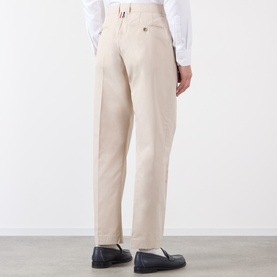 Model wearing Thom Browne Tapered Pressed-Crease Chinos in beige, rear view, styled with a white shirt and navy loafers.