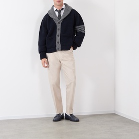 Model wearing Thom Browne Tapered Pressed-Crease Chinos in beige, styled with a navy varsity cardigan, white shirt and black loafers.
