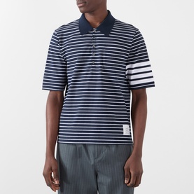 Model wearing Thom Browne navy and white striped cotton polo with signature 4-bar sleeve detail and spread collar, styled with grey trousers.
