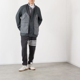 Model wearing Thom Browne 4-Bar Colourblock Sweat Pants in dark grey with iconic white 4-bar stripe detail, styled with a grey pinstripe blazer and