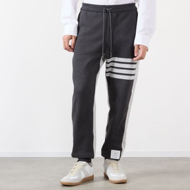 Model wearing Thom Browne 4-Bar Colourblock Sweat Pants in dark grey with white 4-bar stripe detail, styled with white trainers.