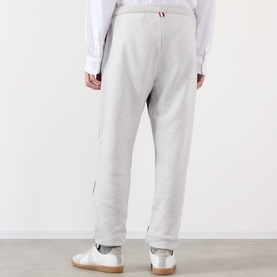 Model wearing Thom Browne 4-Bar Colourblock Sweat Pants in dark grey, rear view, with white trainers and white shirt.