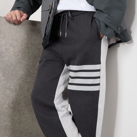 Model wearing Thom Browne 4-Bar Colourblock Sweat Pants in dark grey with light grey 4-bar stripe detail and elasticated drawstring waist.