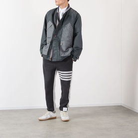 Model wearing Thom Browne 4-Bar Colourblock Sweat Pants in dark grey with white 4-bar stripe detail, styled with grey jacket and white trainers.