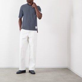 Model wearing Thom Browne navy and white cotton striped T-shirt, styled with white wide-leg trousers and dark loafers.
