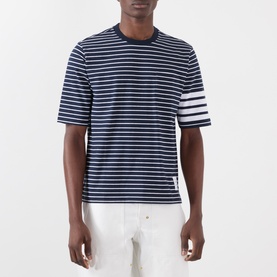 Model wearing Thom Browne navy and white striped cotton T-shirt with signature four-bar white armband detail, styled with white trousers.