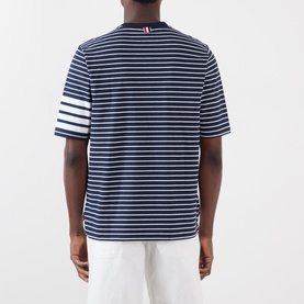 Model wearing Thom Browne navy and white striped cotton T-shirt, back view, with signature four-bar stripe detail on left sleeve.