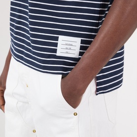 Model wearing Thom Browne navy and white striped cotton T-shirt with logo tab, styled with white trousers with gold-tone buttons.