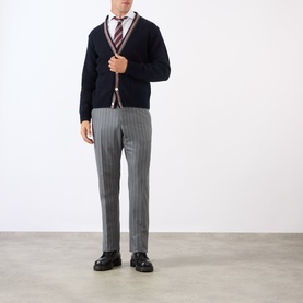 Model wearing Thom Browne Back Strap Pinstripe Trousers in medium grey wool, slim-leg fit. Styled with navy cardigan and striped tie.