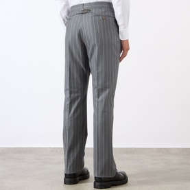 Model wearing Thom Browne Back Strap Pinstripe Trousers in medium grey wool, slim-leg fit, rear strap detail, styled with white shirt and black shoes.