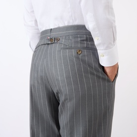 Model wearing Thom Browne Back Strap Pinstripe Trousers in medium grey wool, rear view showing adjustable back strap and jetted pockets, styled with