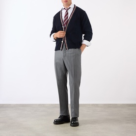 Model wearing Thom Browne Back Strap Pinstripe Trousers in medium grey wool, slim-leg, styled with navy cardigan and black loafers.