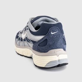 Nike trainer in Thunder Blue and Sail, featuring mesh and suede upper, white swoosh logo, and cream midsole. Rear three-quarter view.