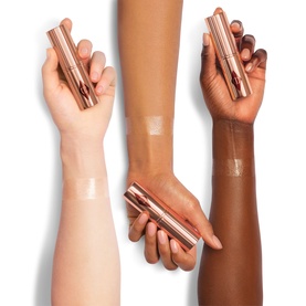 Charlotte Tilbury Unreal Highlighter Stick in Glazed Goddess swatched across three arm skin tones, showing rose-gold shimmer finish