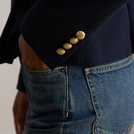 Model wearing Lauren navy blazer, close-up of gold button detail at cuff, styled with mid-wash denim jeans.