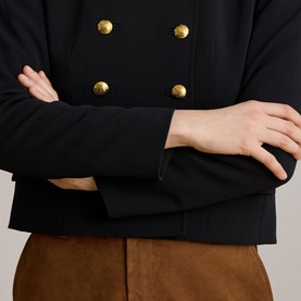 Model wearing Lauren black blazer with gold double-breasted buttons, styled with tan suede skirt, arms crossed detail view.