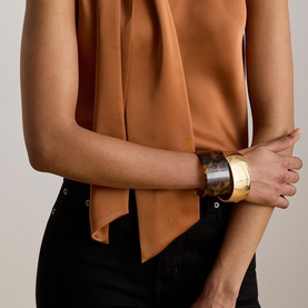Model wearing Lauren Red Terracotta sleeveless tie-neck blouse, styled with black trousers and gold-tone cuff bracelets.