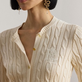 Model wearing Lauren Mascarpone Cream cable-knit cardigan with gold monogram logo buttons, styled with gold snake earrings